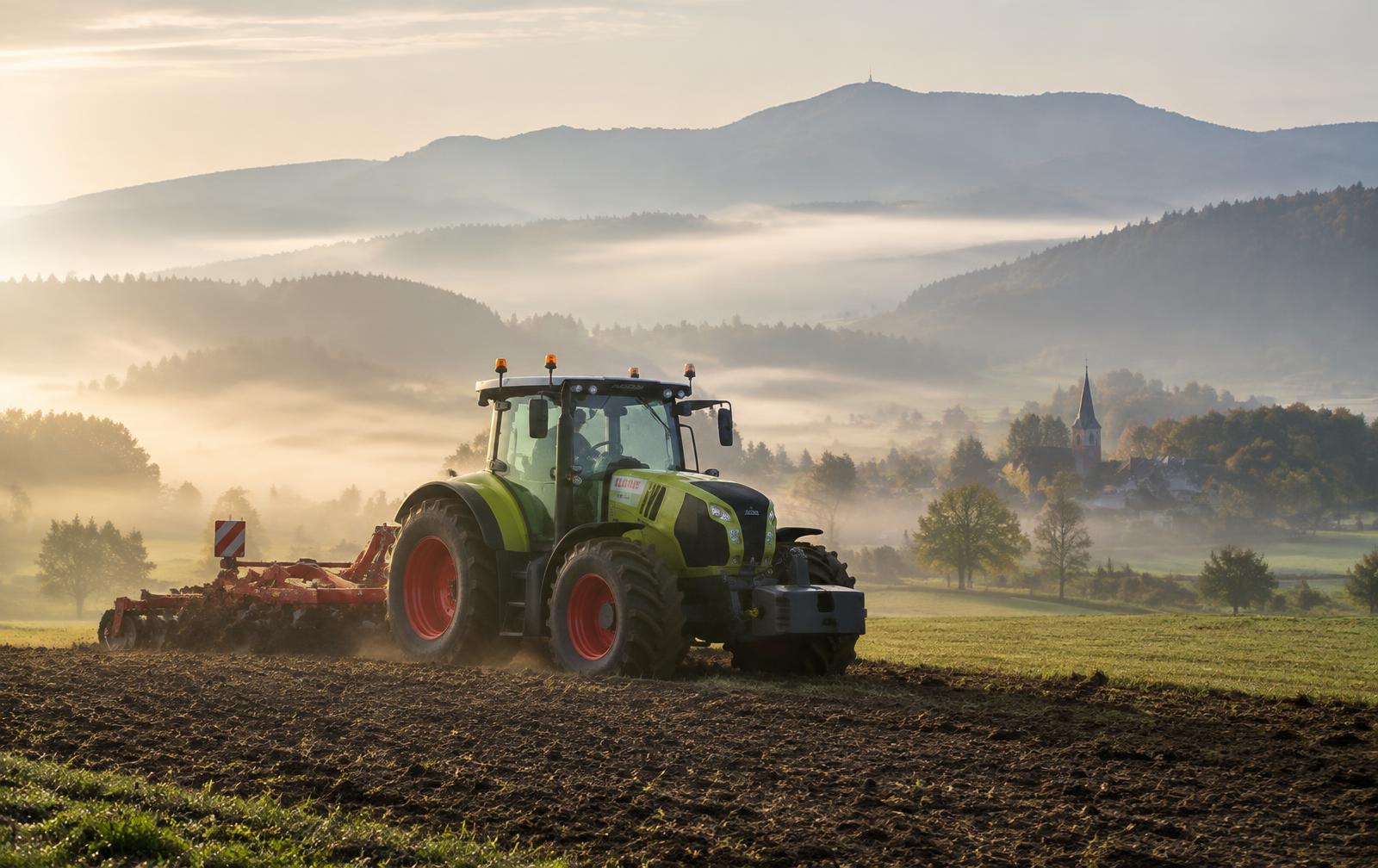 Tracteur au travail dans un champ, collines vosgiennes dans la brume matinale